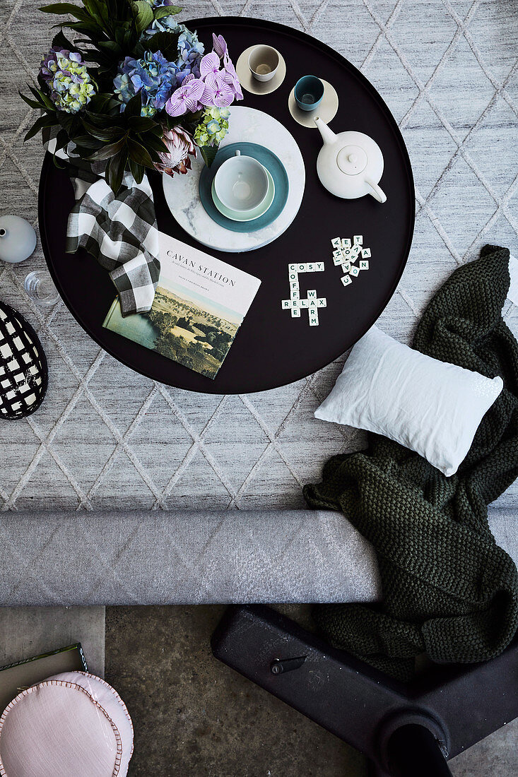 Black side table with tea set, flowers, book and Scrabble