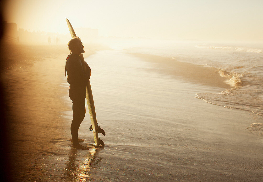 Surfer standing with board on beach