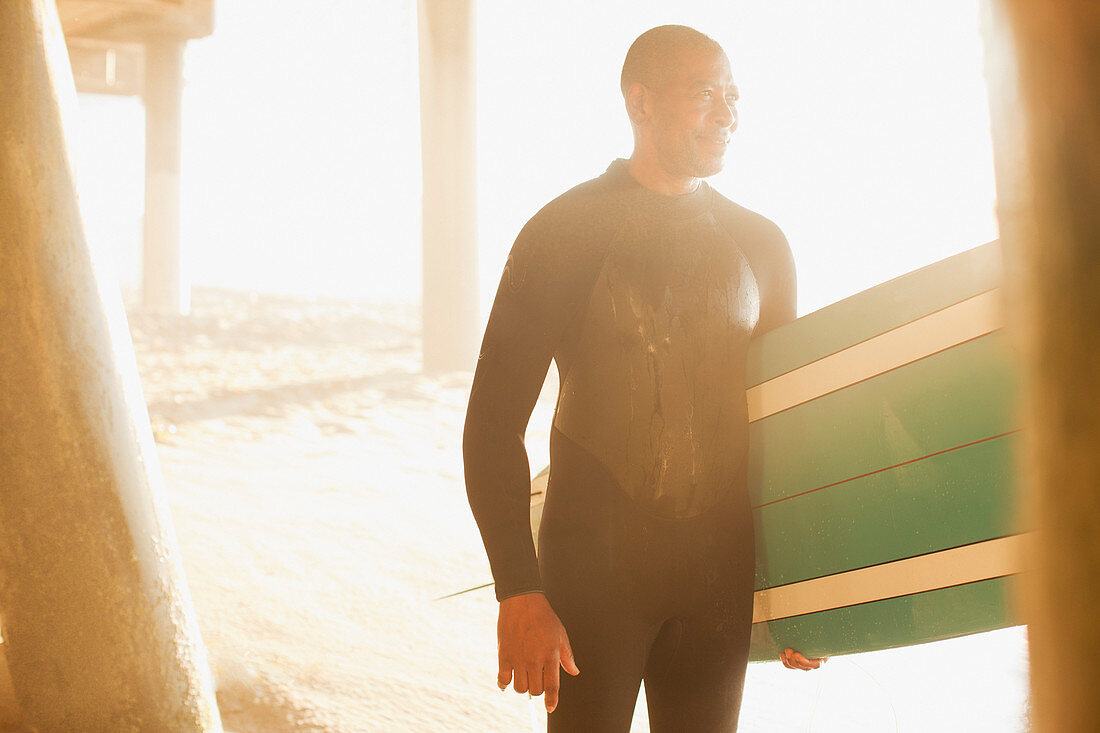 Older surfer carrying board under pier