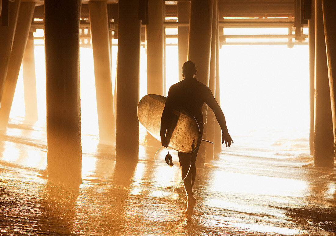 Older surfer carrying board under pier