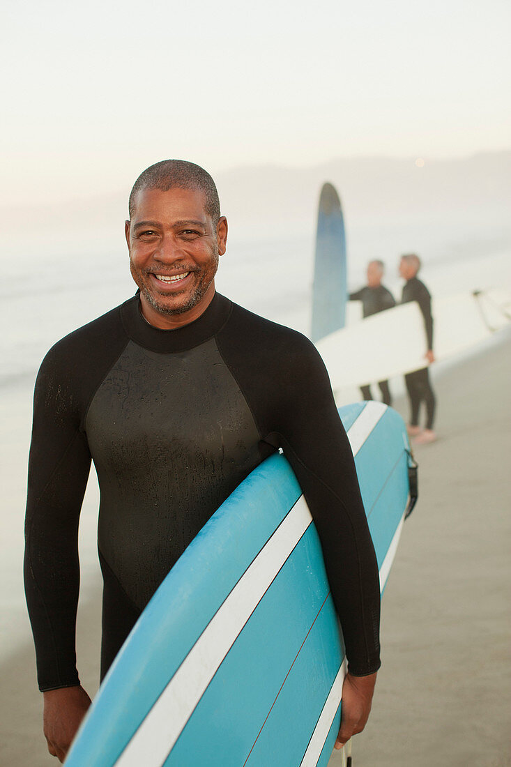 Older surfer carrying board on beach