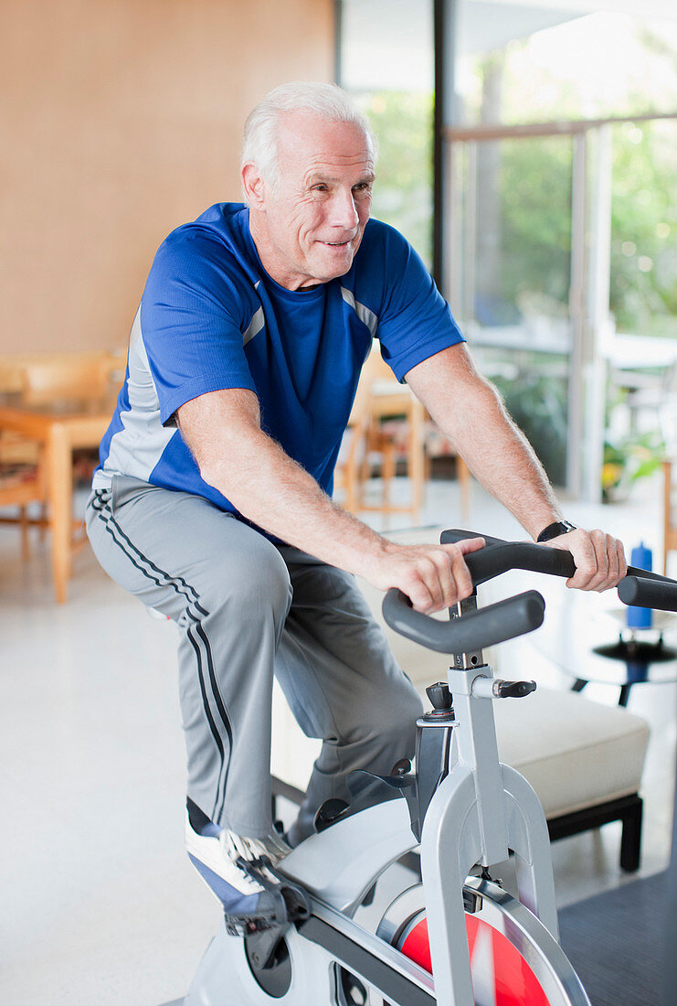 Older man riding exercise bike at home