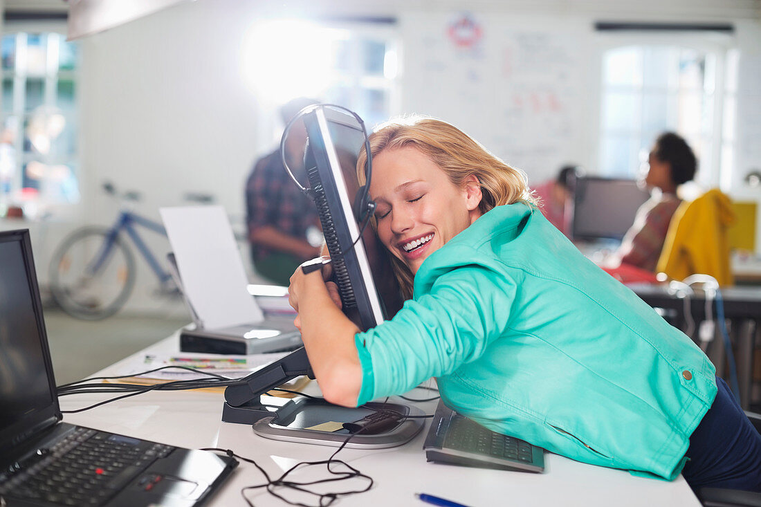 Businesswoman hugging computer at desk