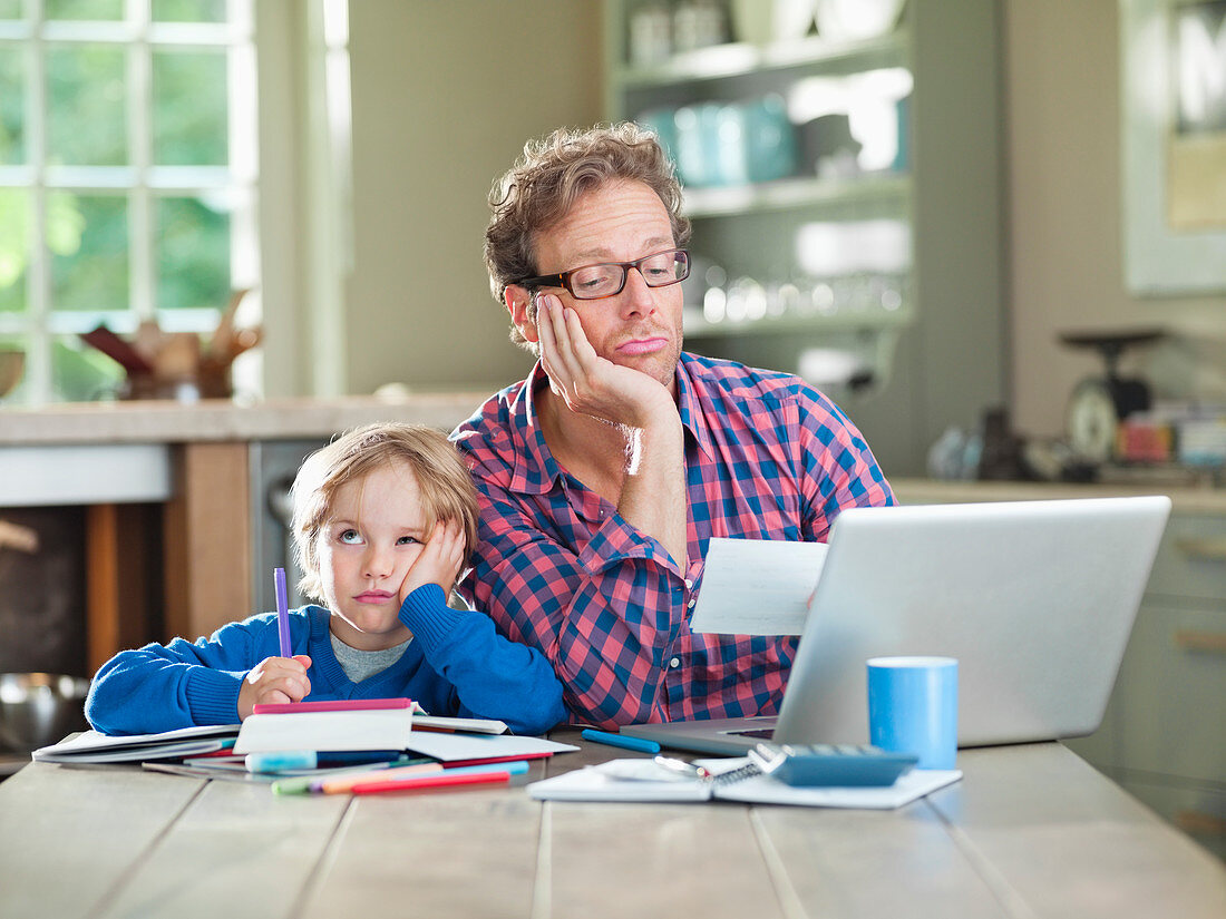 Bored father and son working at table