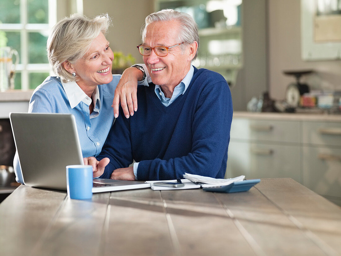 Couple using laptop at kitchen table