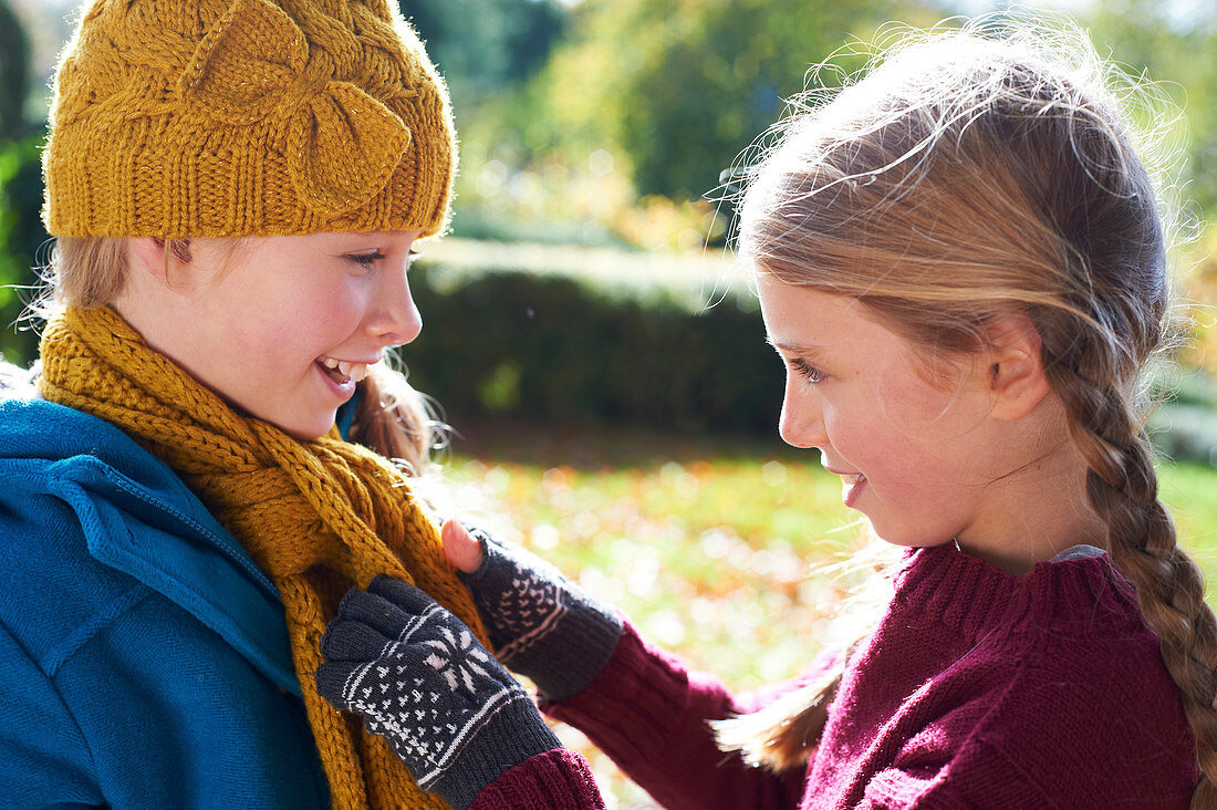 Girl tying sister's scarf outdoors