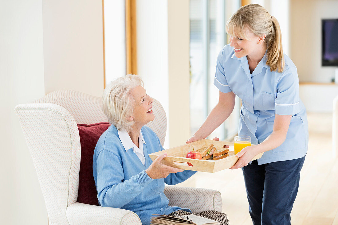 Caregiver giving older woman tray of food