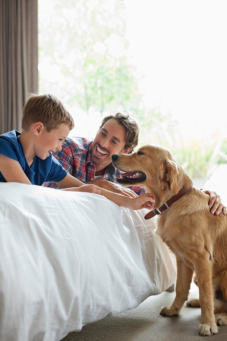 Father and son petting dog in bedroom