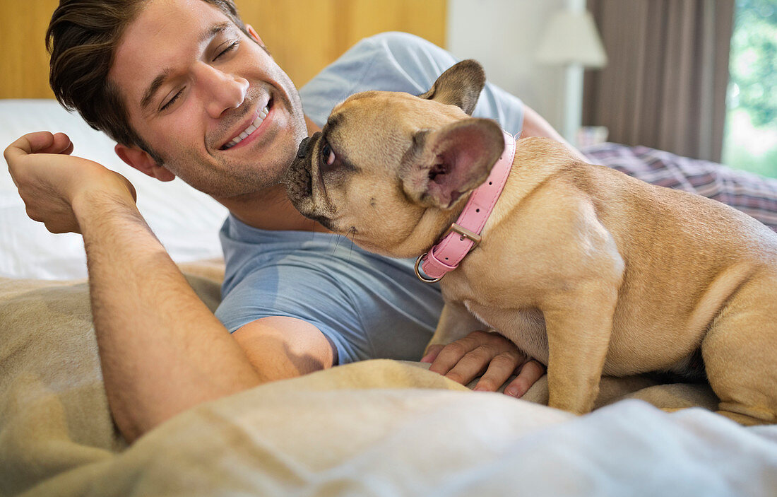 Dog licking man's face on bed
