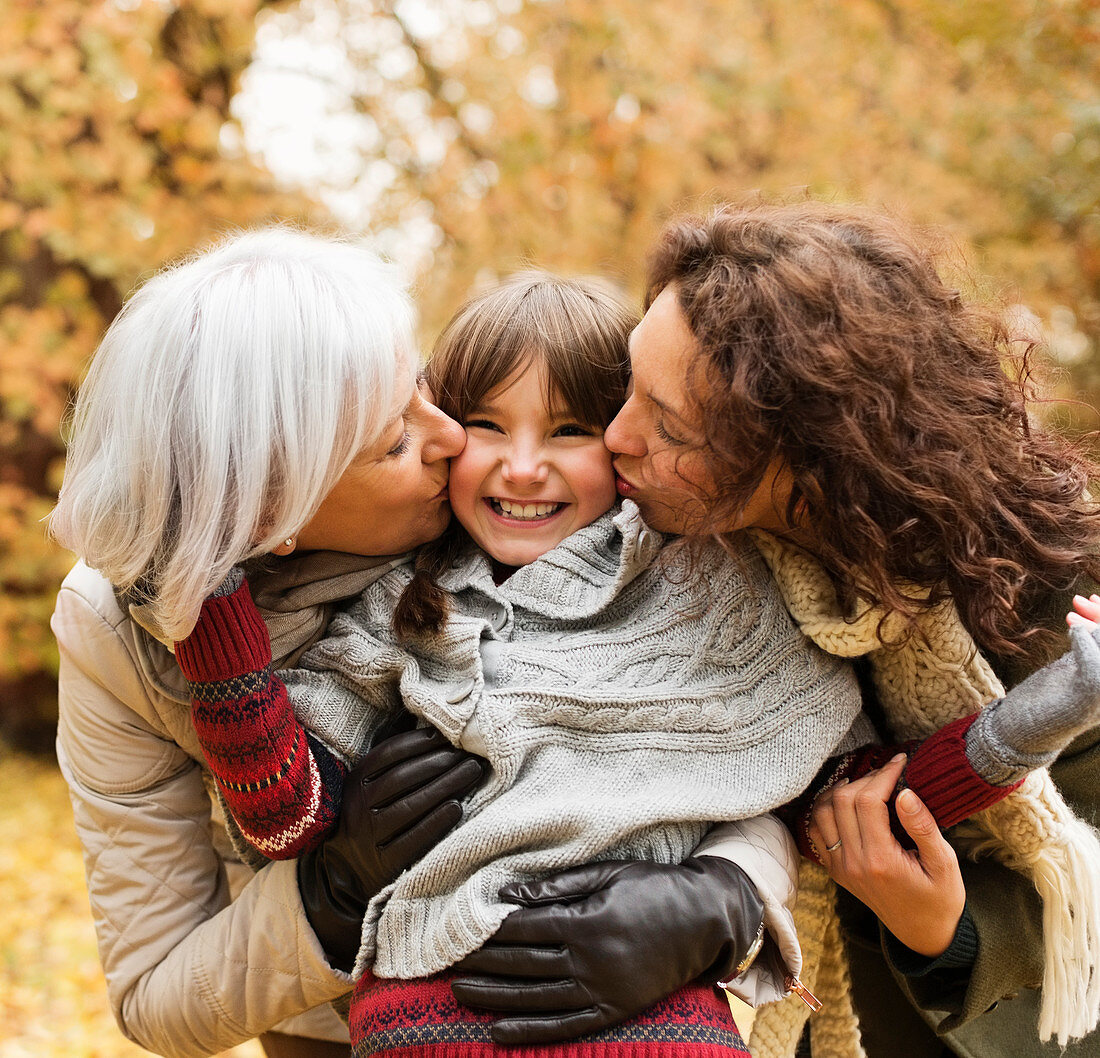 Woman and daughter kissing girl in park