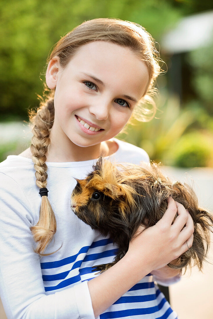 Smiling girl holding guinea pig outdoors