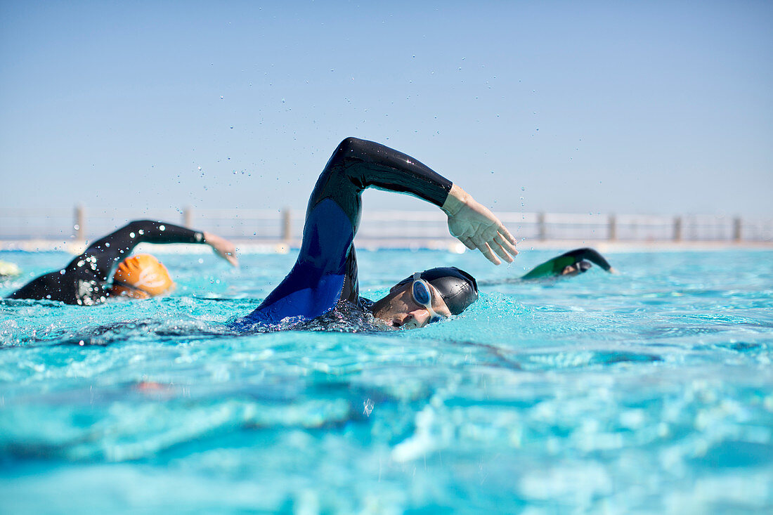 Triathletes in wetsuits racing in pool