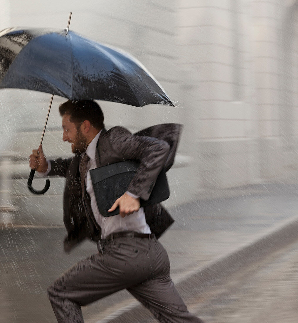 Businessman with umbrella running in rain