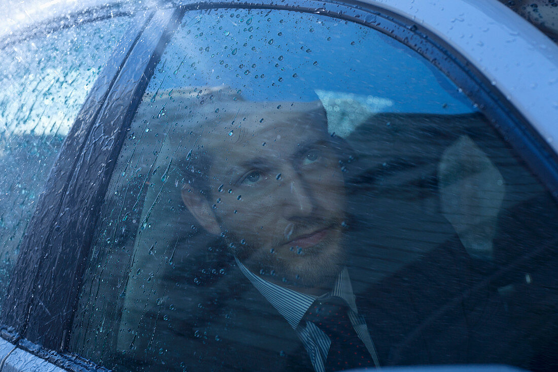 Businessman in car looking up at rain