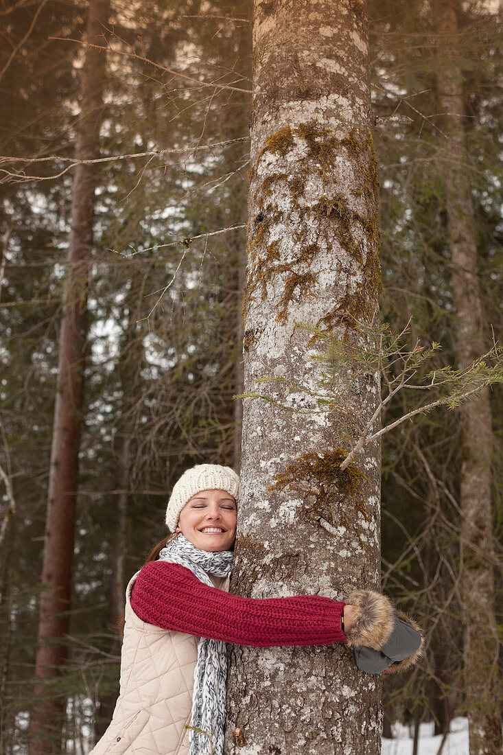 Happy woman hugging tree trunk in woods