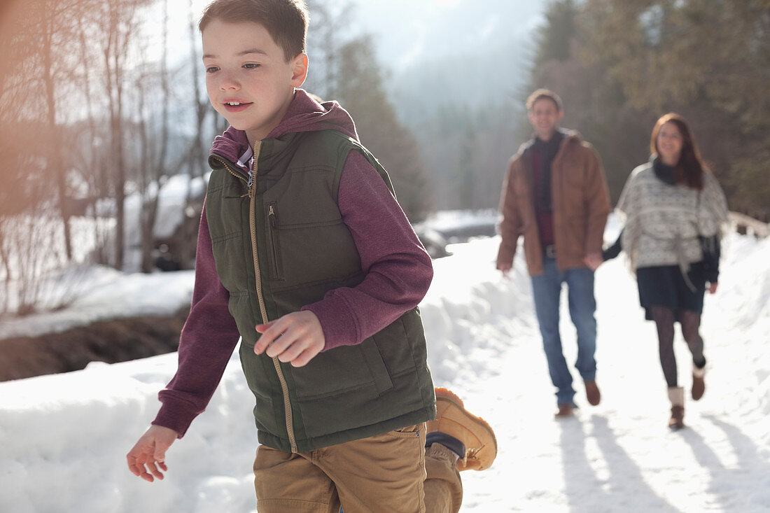 Parents watching boy run in snowy lane