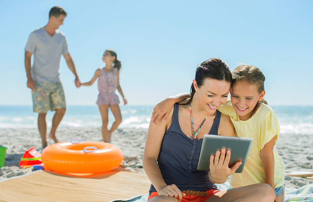 Mother and daughter using tablet on beach