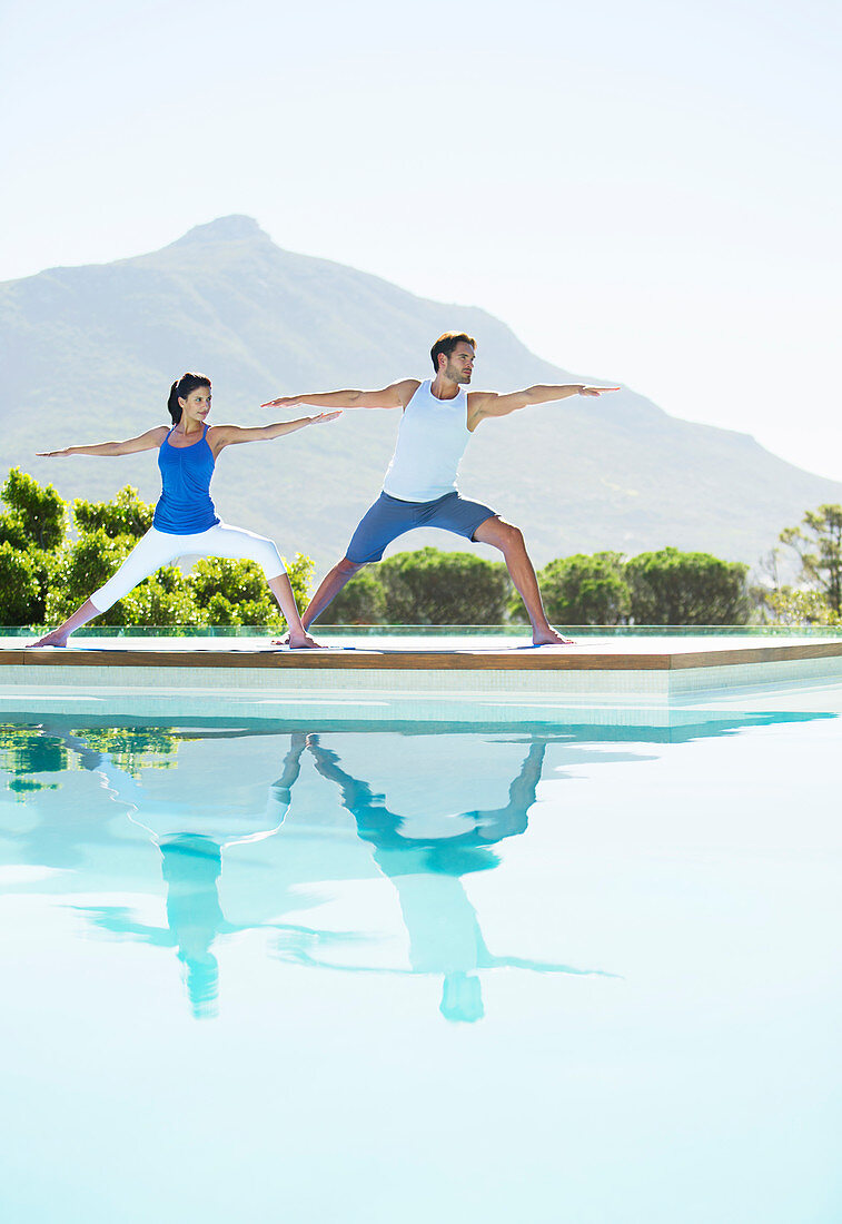 Couple practicing yoga at poolside