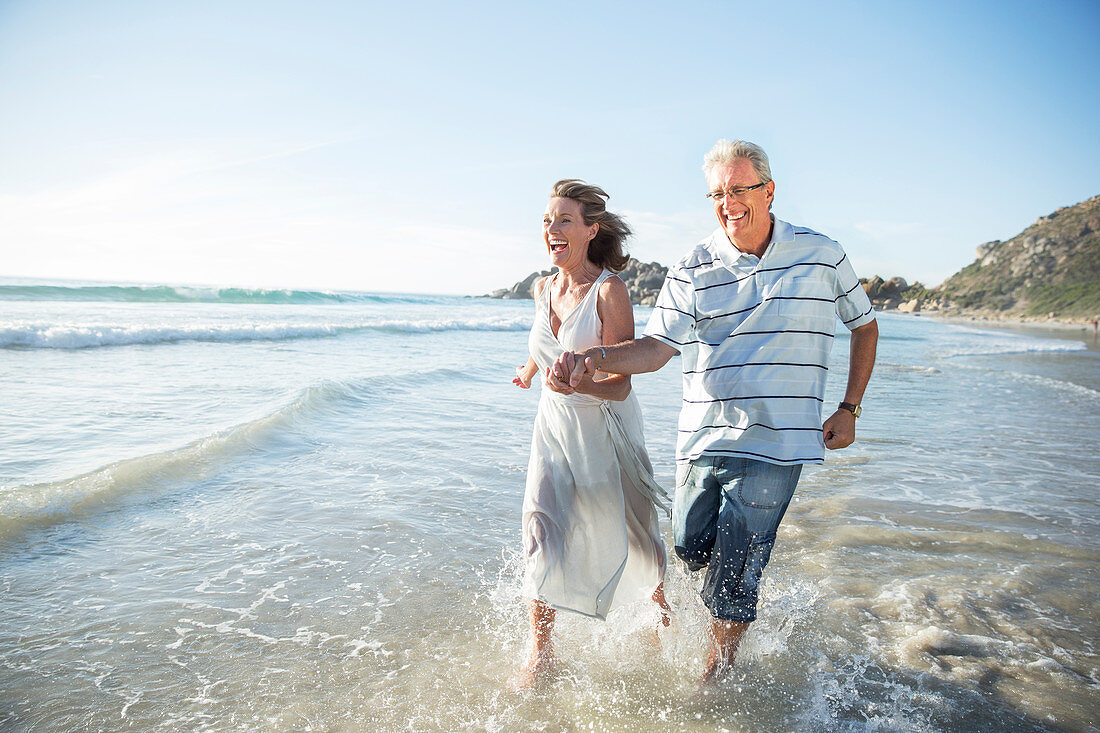 Older couple playing in waves on beach