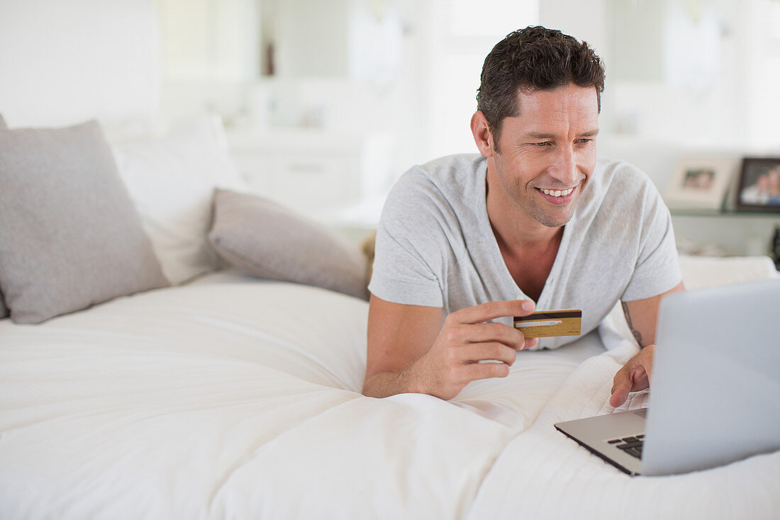 Man shopping online with laptop on bed