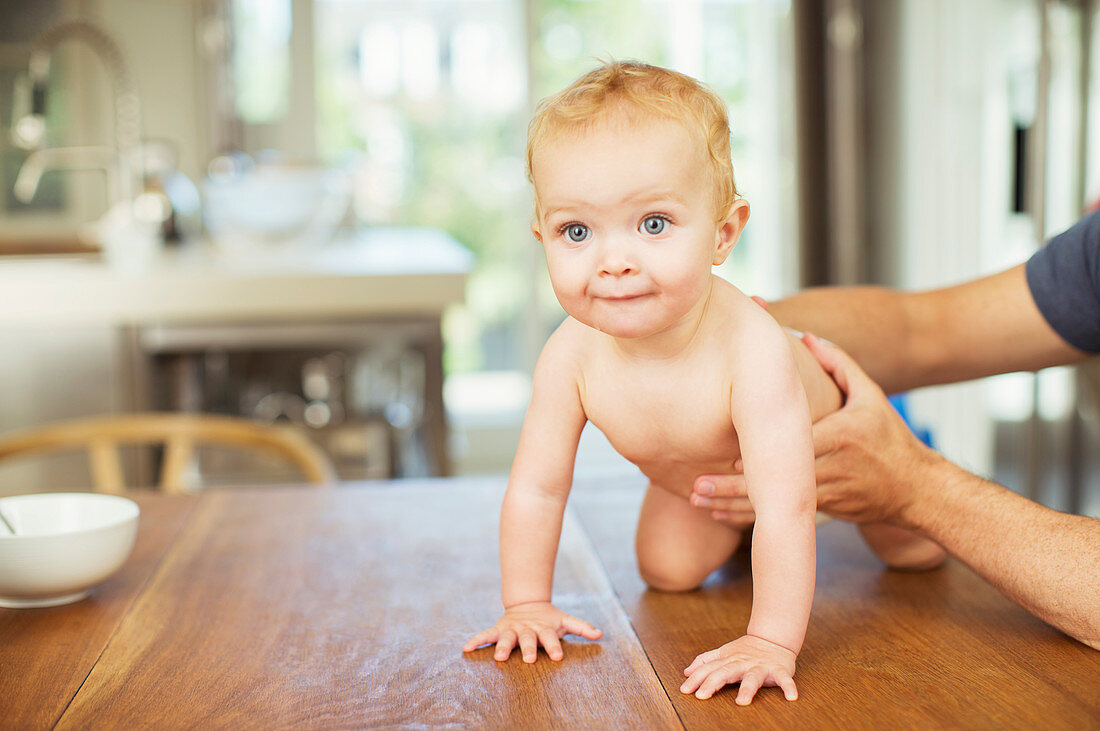 Father helping baby crawl on table