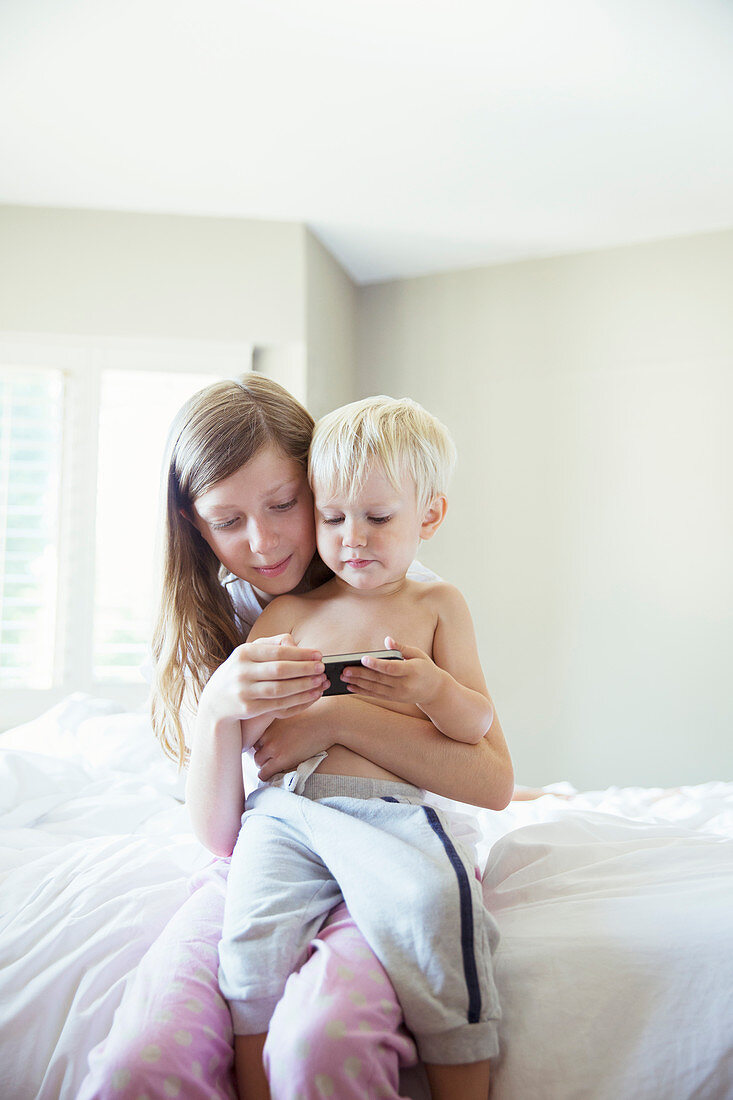 Children using cell phone together on bed