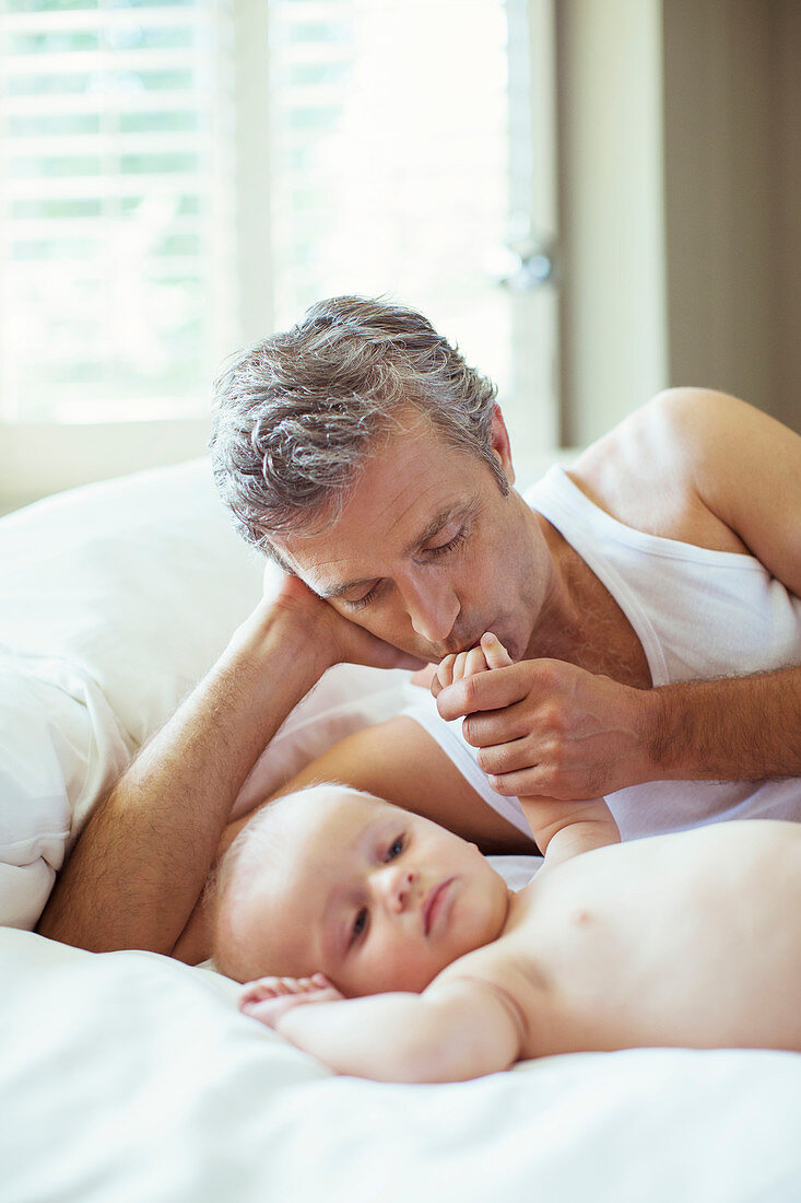 Father kissing baby's hand on bed