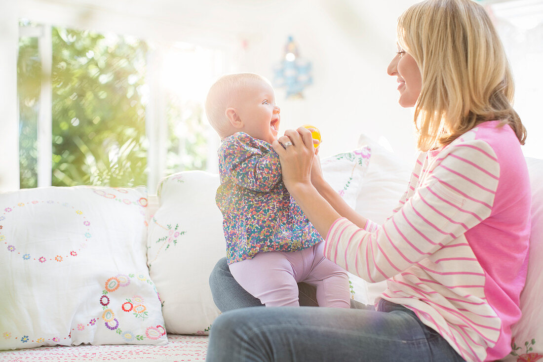 Mother playing with baby girl on sofa