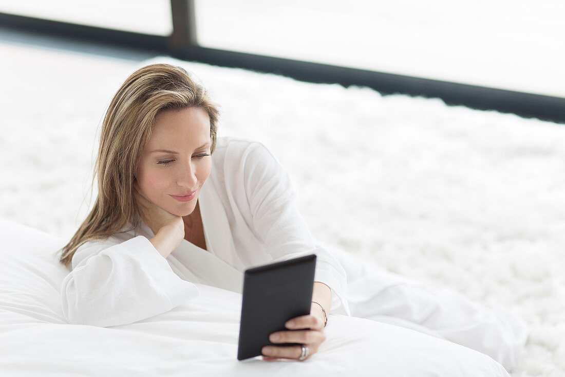 Woman in bathrobe using tablet in bedroom