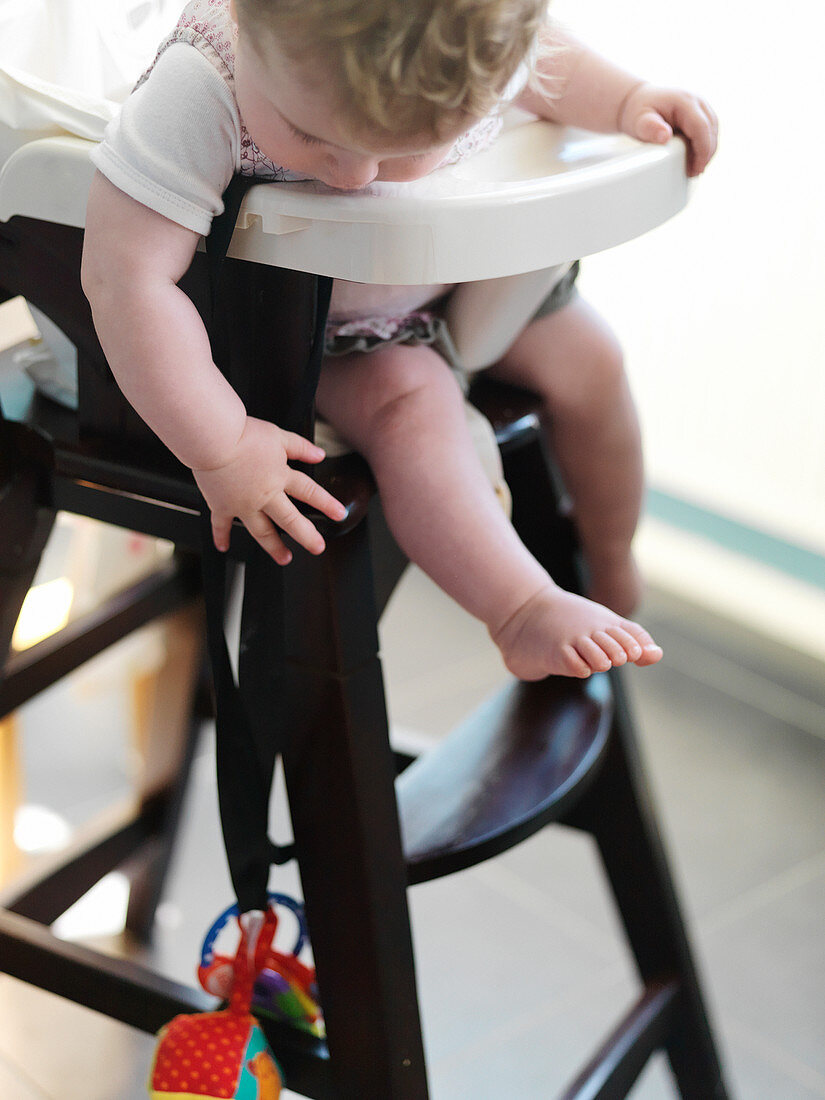 Baby girl in high chair reaching for toy