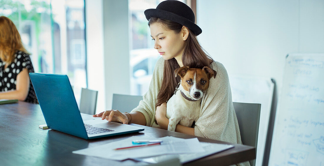 Woman holding dog and working in office
