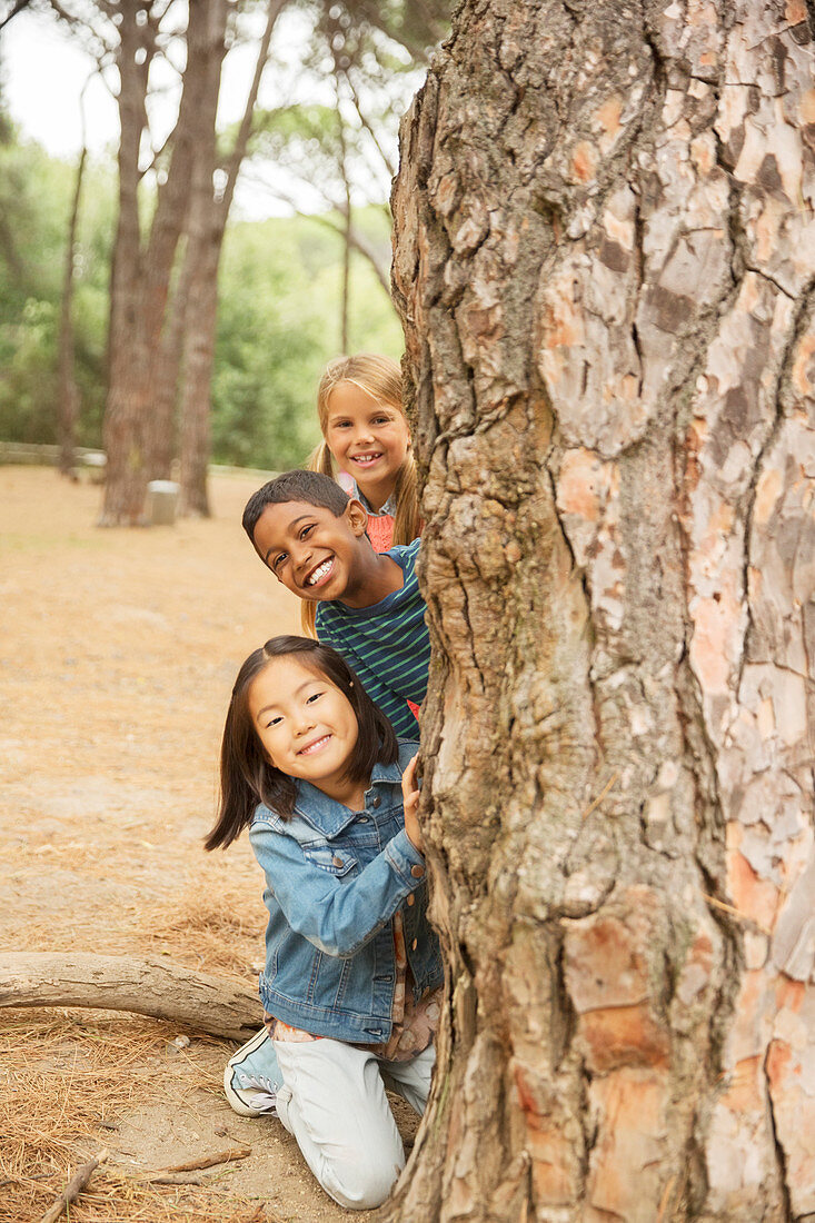 Children peeking out from behind tree
