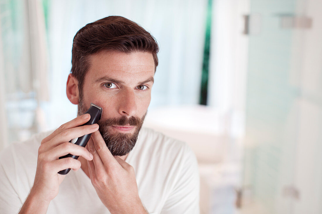 Man trimming beard in bathroom mirror