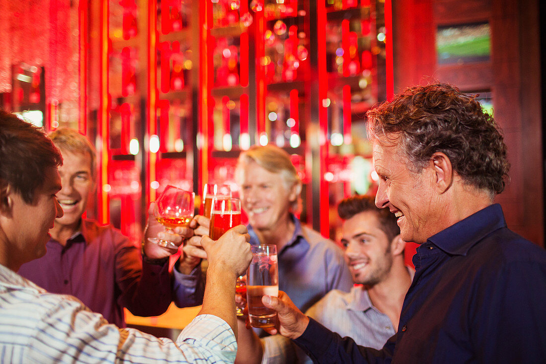 Five smiling men raising toast in bar