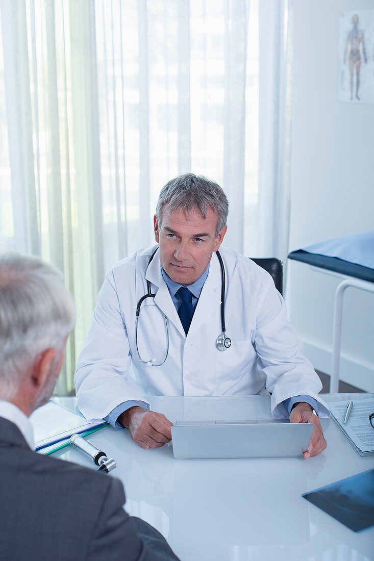 Mature doctor with laptop and man at desk