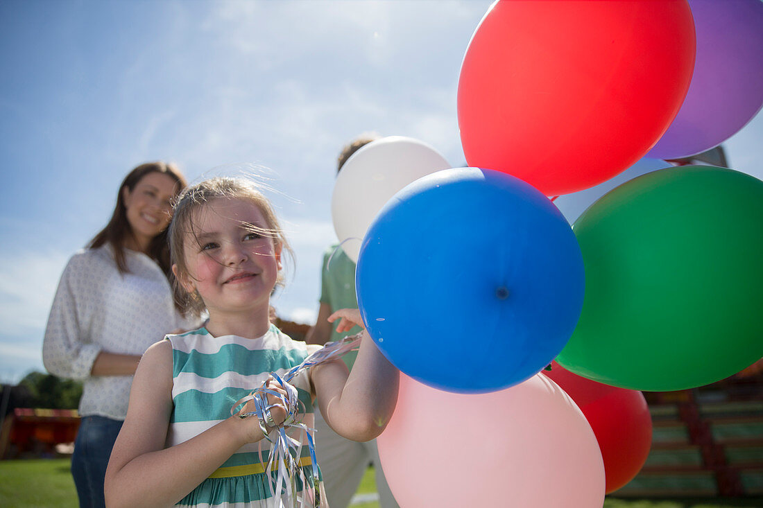 Young girl holding balloons at sunny day