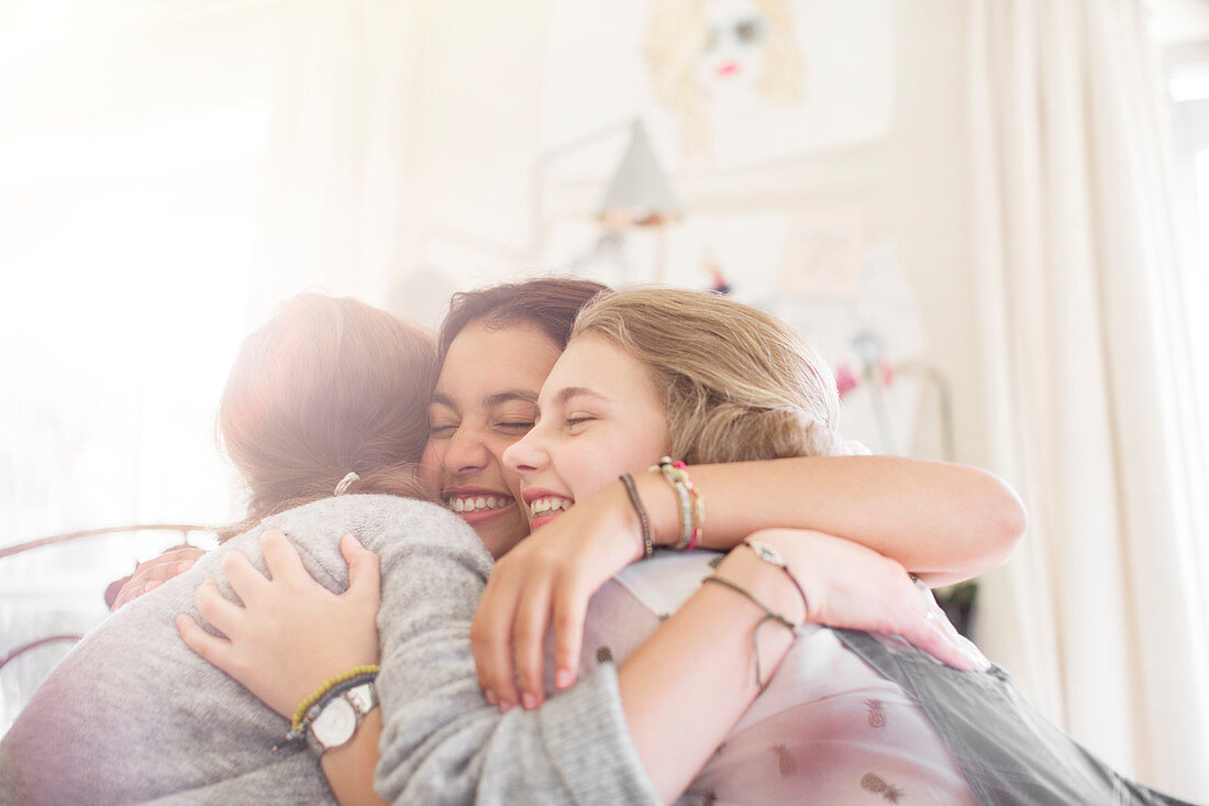 Three teenage girls embracing at home