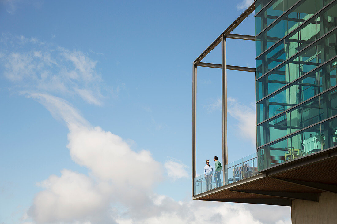 Men talking on balcony of glass bump out against blue sky