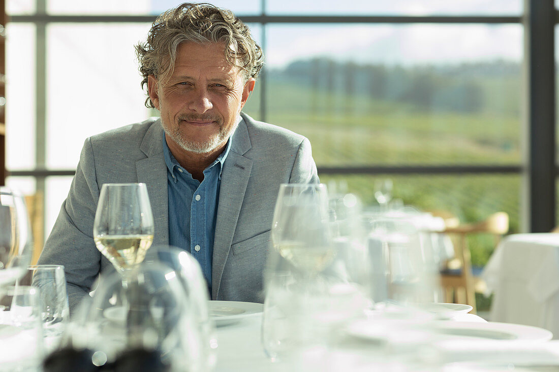Portrait confident man with white wine at sunny restaurant t