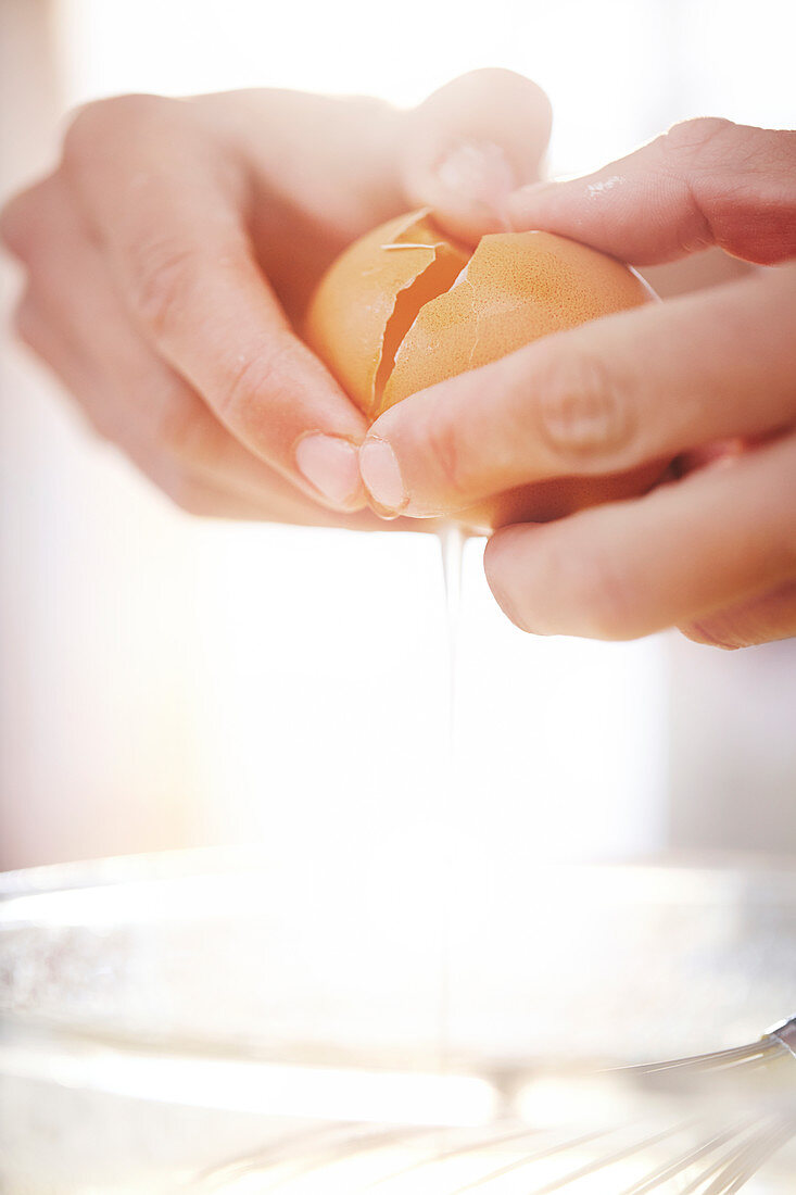 Close up woman cracking egg baking