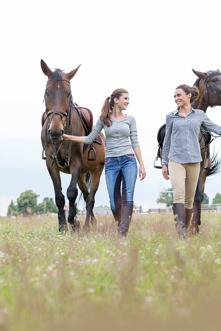 Women walking horses in rural field