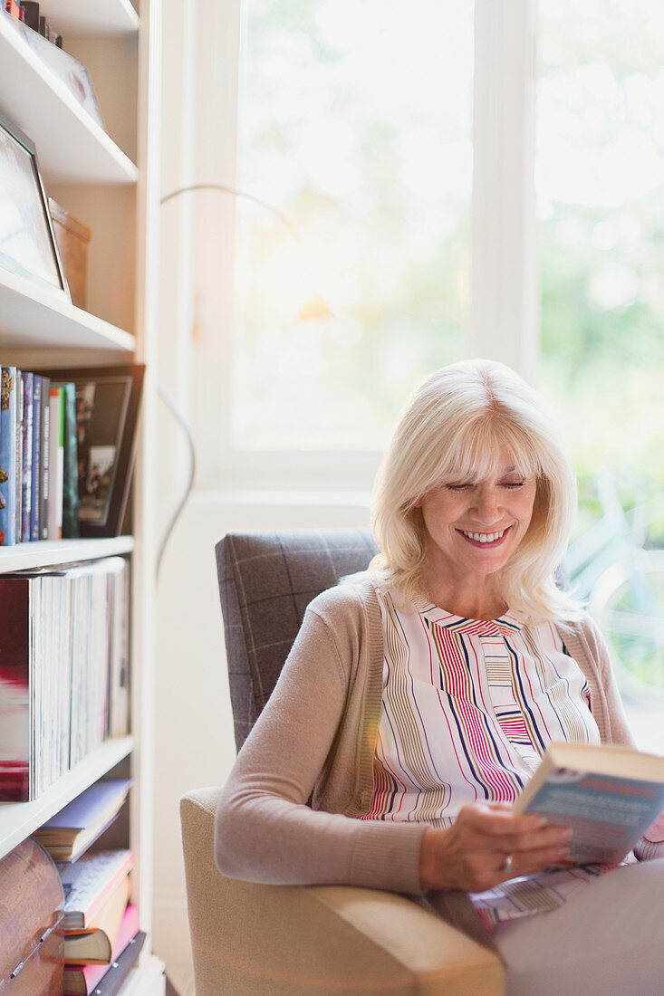 Smiling senior woman reading book in den