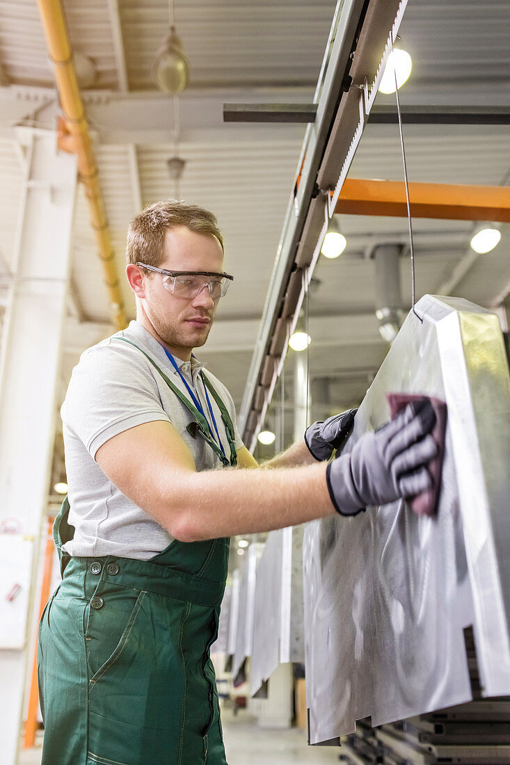 Worker sanding steel part in factory