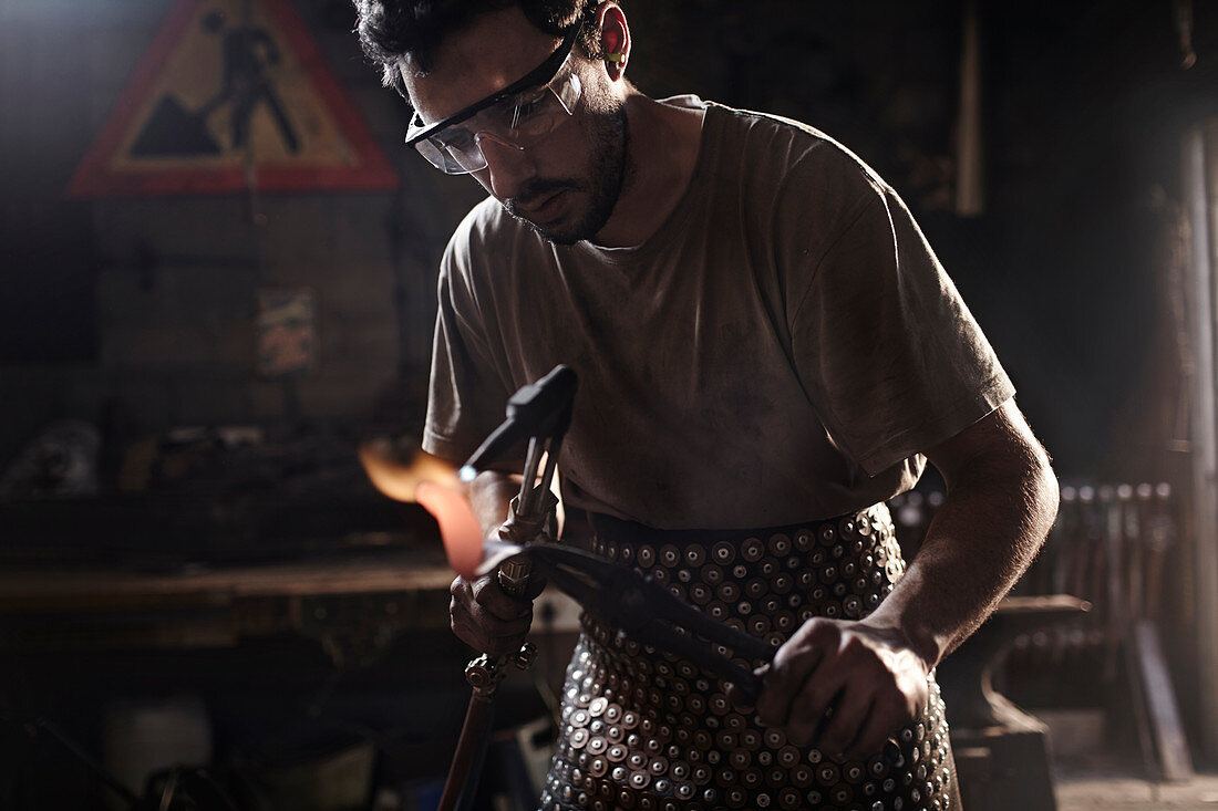 Blacksmith using blowtorch in forge