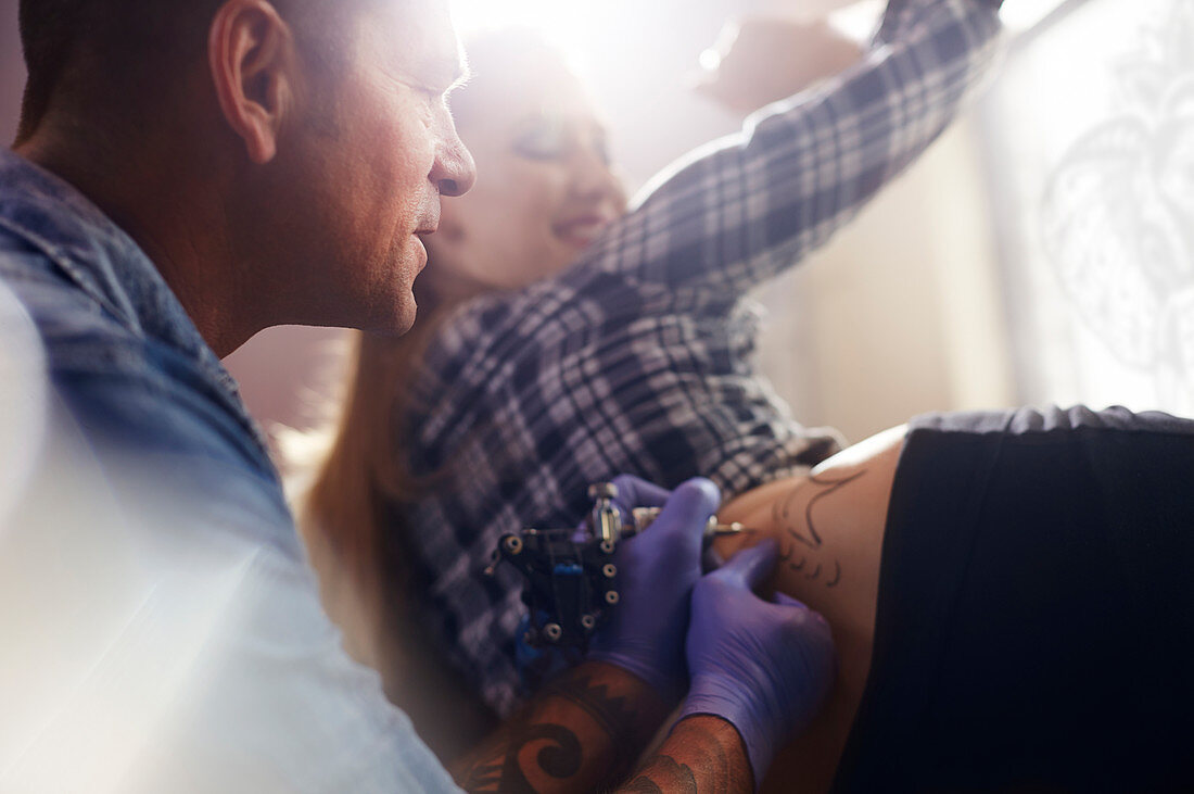 Tattoo artist tattooing woman's hip