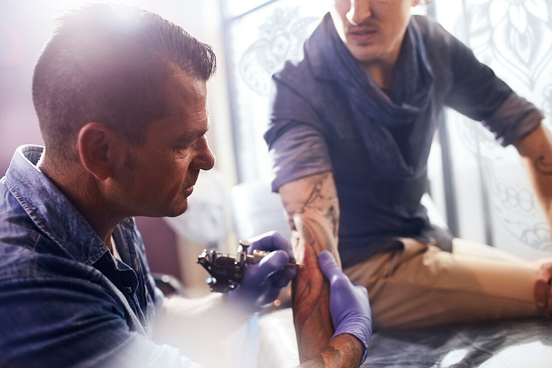 Tattoo artist tattooing man's forearm