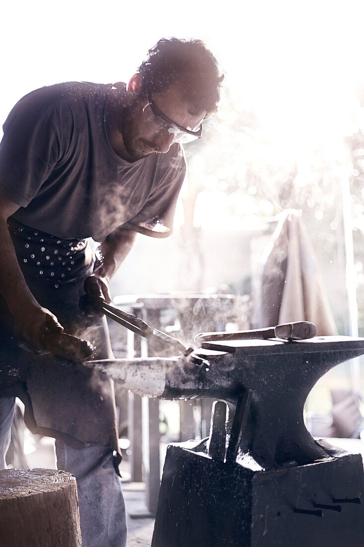 Blacksmith shaping iron over anvil