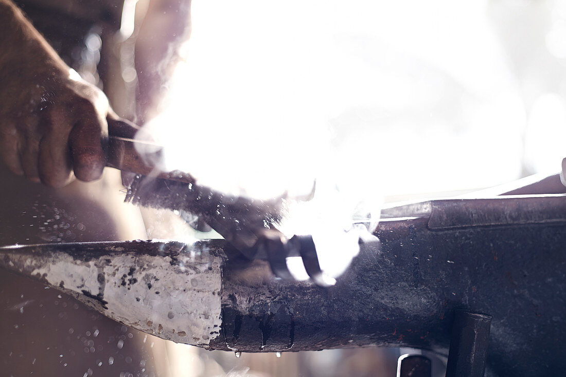 Blacksmith brushing iron tool over anvil