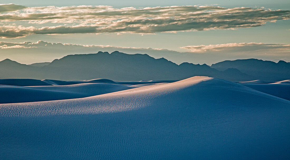Silhouetted mountains behind sand dune