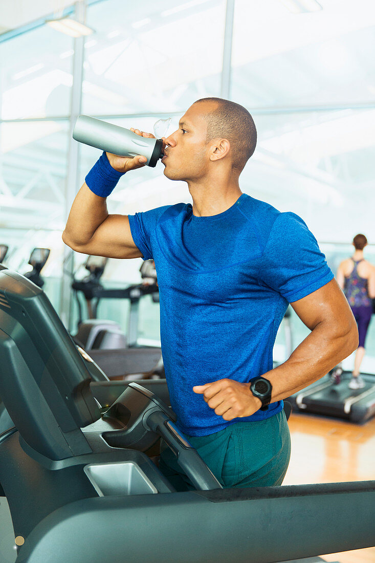 Man drinking water on treadmill at gym